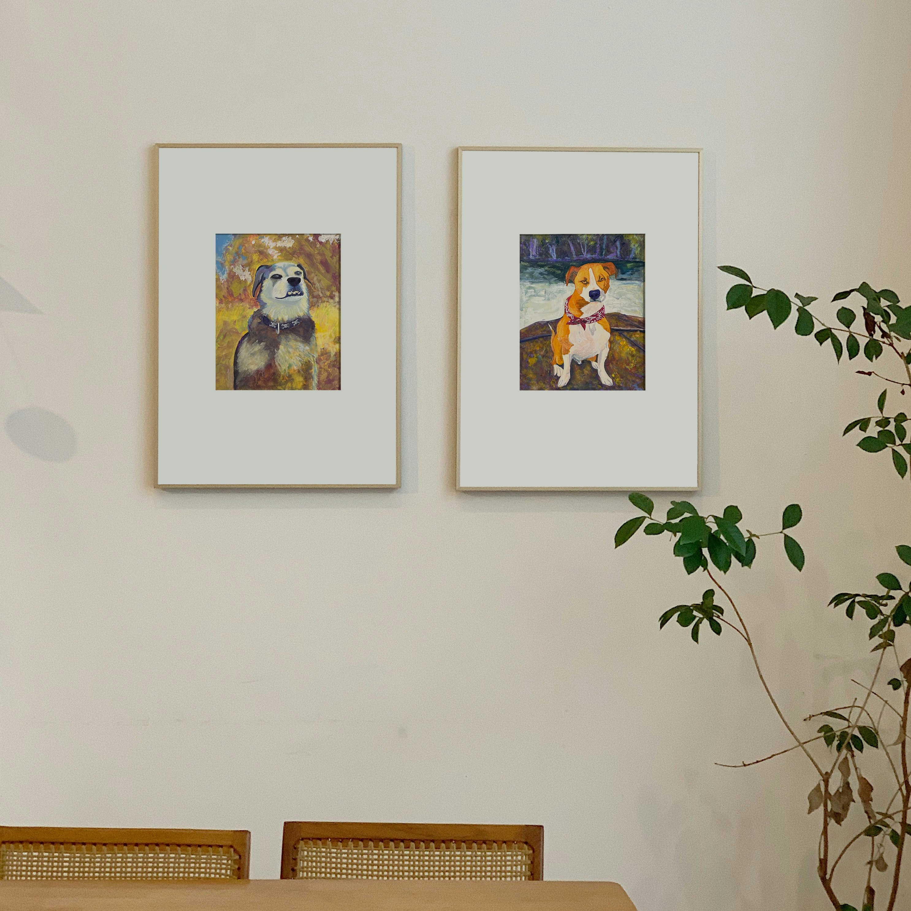 Two framed artworks of dogs on a wall with a plant in the corner.